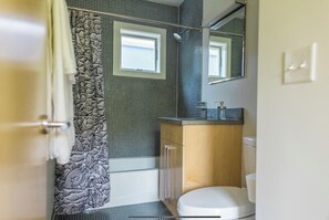 A bathroom with a shower curtain featuring a dragon design, a toilet, a sink with a mirror above it, and a window above the toilet.