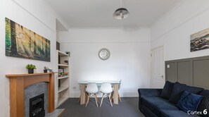 A living room with a fireplace, a dining table with chairs, a sofa, and a clock on the wall.
