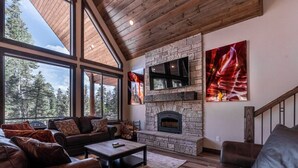 Un salón amplio con chimenea de piedra, sofás de cuero y ventanas grandes que ofrecen vistas a árboles.