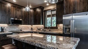 Una cocina moderna con armarios de madera oscura, encimera de granito, electrodomésticos de acero inoxidable y un amplio ventanal que proporciona luz natural.