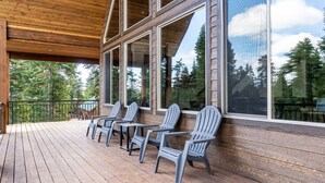 Una terraza de madera con sillas Adirondack y ventanas amplias que dan a un área boscosa.