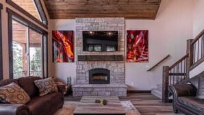 Un salón con chimenea de piedra, un televisor encima y dos grandes cuadros abstractos.