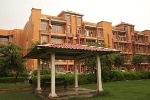 A multi-story building with a covered outdoor seating area, surrounded by greenery and parked cars.