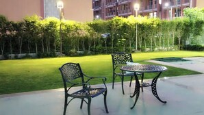 An outdoor seating area with metal chairs and a table, surrounded by a well-maintained lawn and hedges, with a building in the background. - Explore Rajasthan's rich cultural heritage in NCR (Neemrana)