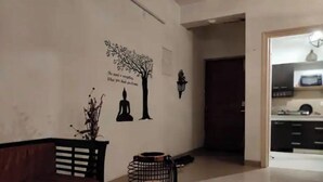 A modern living room with a sofa, a table with a decorative item, and a wall with a tree and meditative figures. - Explore Rajasthan's rich cultural heritage in NCR (Neemrana)