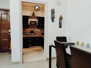 A kitchen with dark cabinets, a tiled backsplash, and a dining area with a table and chairs. - Explore Rajasthan's rich cultural heritage in NCR (Neemrana)