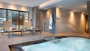 A modern spa area with a hot tub, two lounge chairs, and a glass wall providing a view of the city.