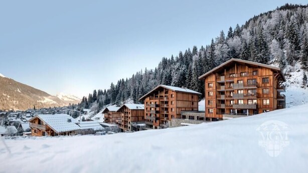 A snow-covered mountain lodge with multiple wooden buildings, including a large multi-story structure with balconies.