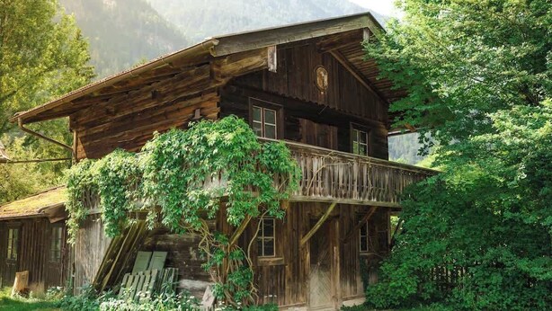 A rustic wooden cabin with a balcony, surrounded by lush greenery and mountains in the background. - Cozy mountain loft - 15 minutes from Garmisch (Oberau)
