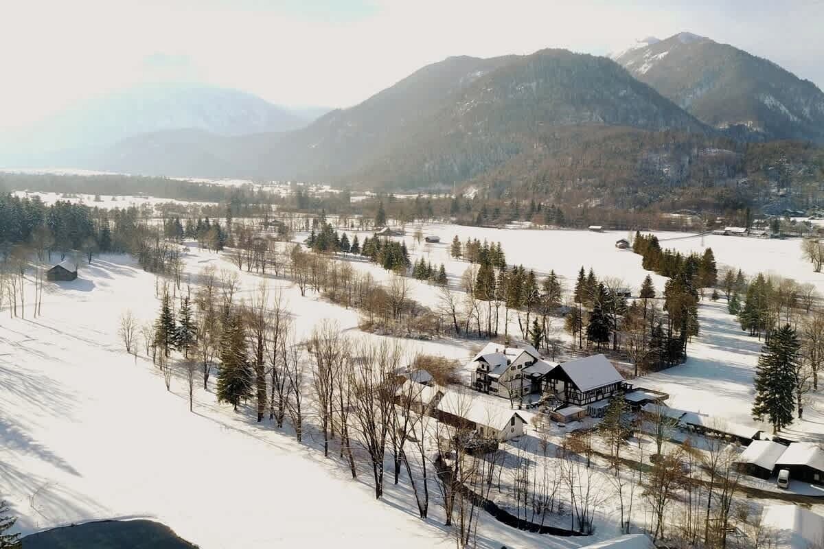 A snow-covered landscape with a large house surrounded by trees and a lake.