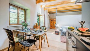 A modern kitchen with wooden beams, a dining area with chairs and a table, and a view of the outdoors through large windows. - Cozy mountain loft - 15 minutes from Garmisch (Oberau)
