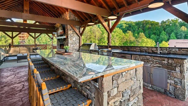 An outdoor kitchen with stone walls, a glass-top bar, and a wooden ceiling.