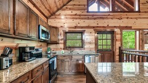 A wooden cabin kitchen with granite countertops, stainless steel appliances, and a large window.