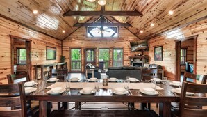 A wooden cabin with a dining area set for four, a ceiling fan, and large windows.