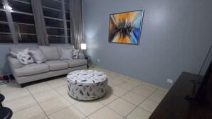 A living room with a grey sofa, a patterned ottoman, and a painting on the wall. - Beautiful apartment at the heart of Condado Beach (San Juan)