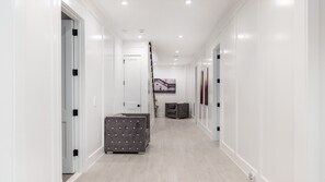 A hallway with white walls, a light wooden floor, and a grey upholstered bench.