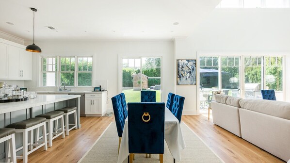 A spacious kitchen with a central island, white cabinetry, and large windows offering a view of the outdoors.