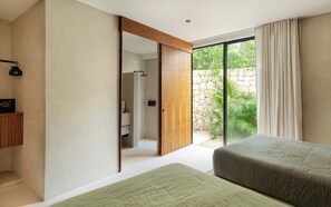 Une chambre moderne dotée d’une grande porte-fenêtre coulissante qui donne sur un mur de pierre et de la verdure. On y trouve un lit recouvert d’une couverture verte, une armoire en bois et une petite table avec une radio.