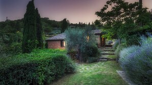 A garden with a brick house, stone pathway, and various shrubs. - Casa di Pan 6, Emma Villas (Panicale)