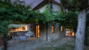 A stone building with a patio area featuring a table and chairs, a stone wall, and a tree. - Casa di Pan 6, Emma Villas (Panicale)