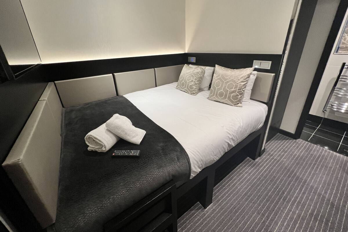 A neatly made bed with a remote control, a rolled towel, and patterned pillows.