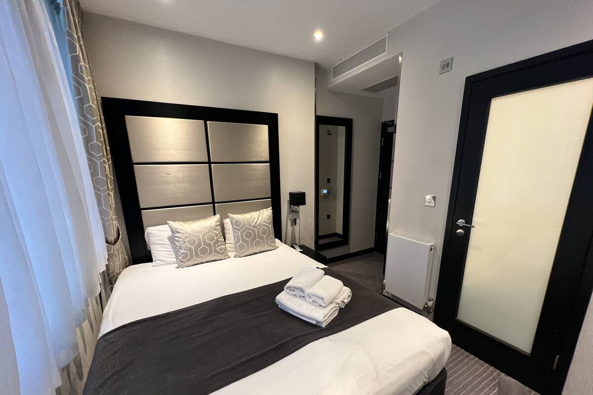 A hotel room with a large bed, a headboard with a geometric pattern, a mirror, and a door.