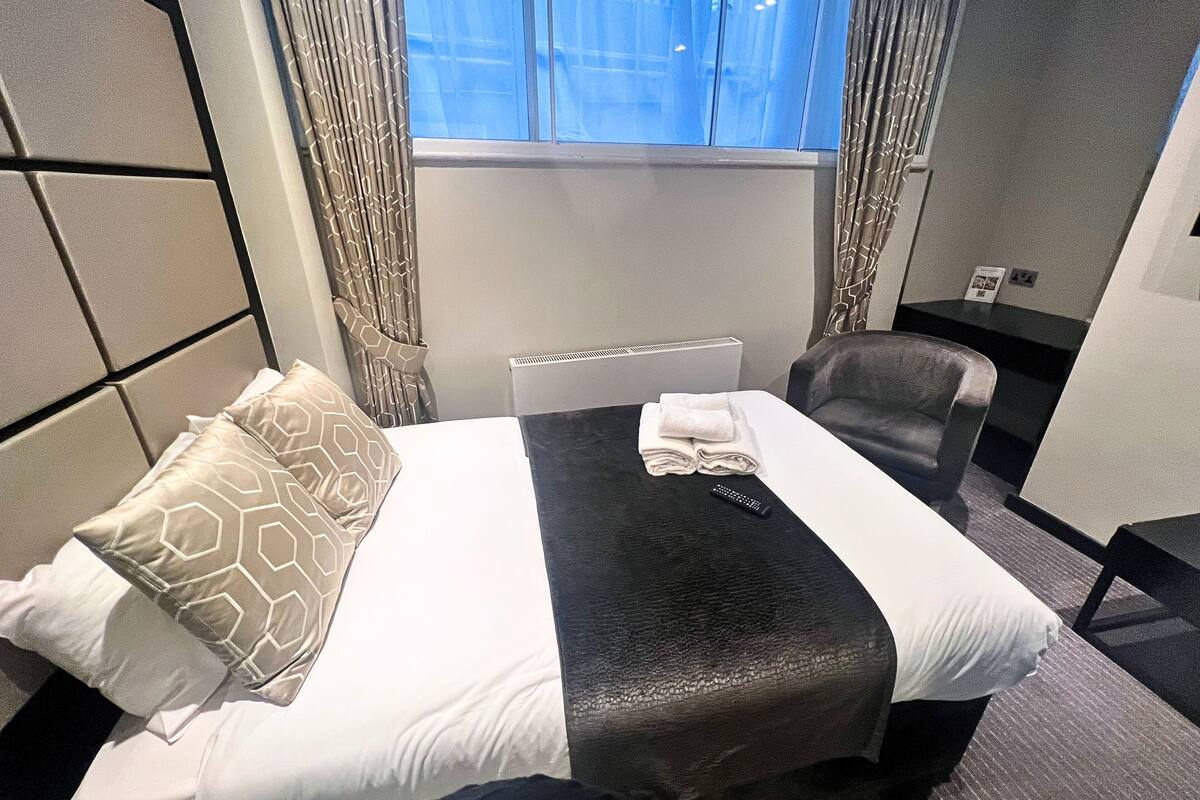 A hotel room with a bed, a chair, a window, and a radiator.