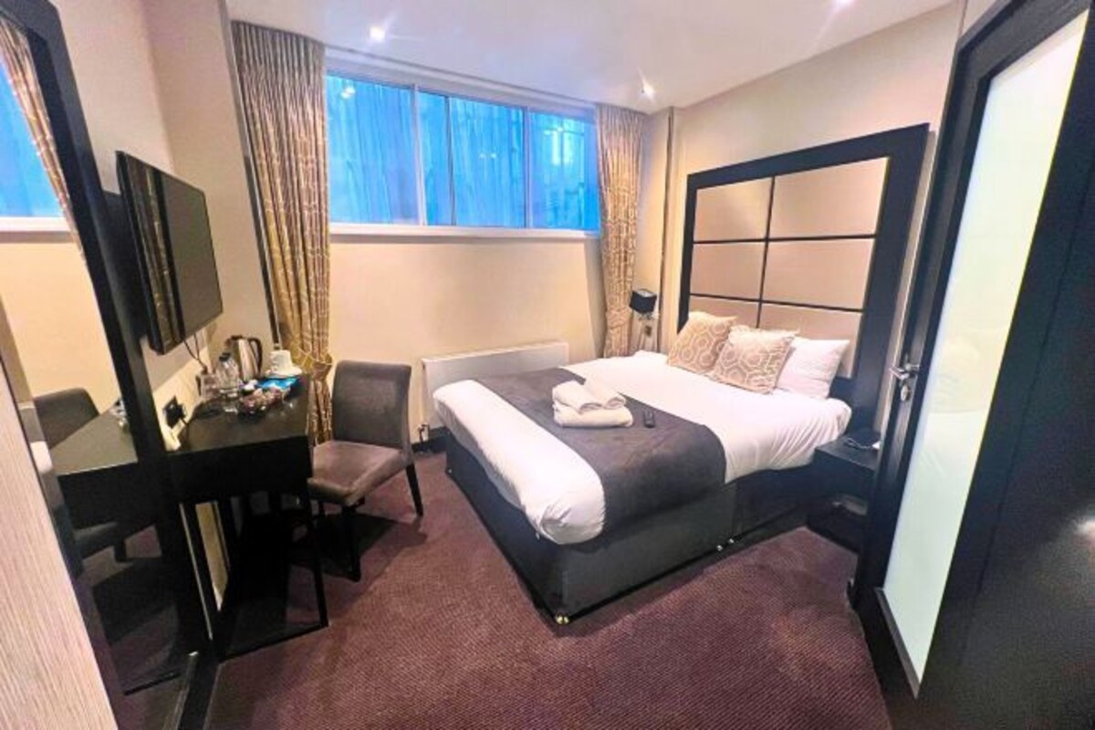 A hotel room with a large bed, a desk with a chair, a TV, and a window with curtains.