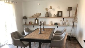 Un coin repas avec une table en bois et quatre chaises, une étagère ornée d’objets décoratifs et une plante en pot.