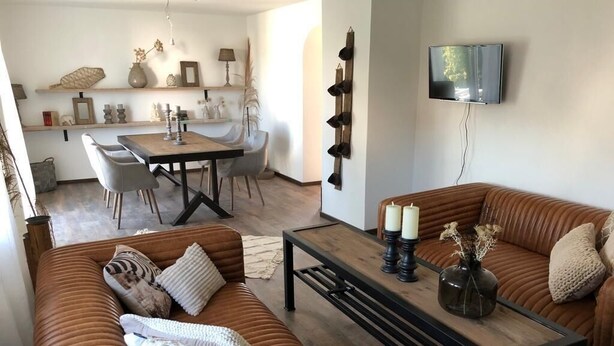 Un salon avec un canapé marron, une table basse en bois et un coin repas comprenant une table et des chaises.