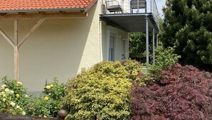 Un bâtiment avec un toit recouvert de tuiles rouges, un balcon doté de balustrades en métal et divers arbustes au premier plan.