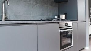 A modern kitchen with a built-in oven, a stainless steel faucet, and a grey tiled backsplash. - VALPOLICELLA APARTMENTS: OLIVE TREE RESIDENCE (Valgatara)