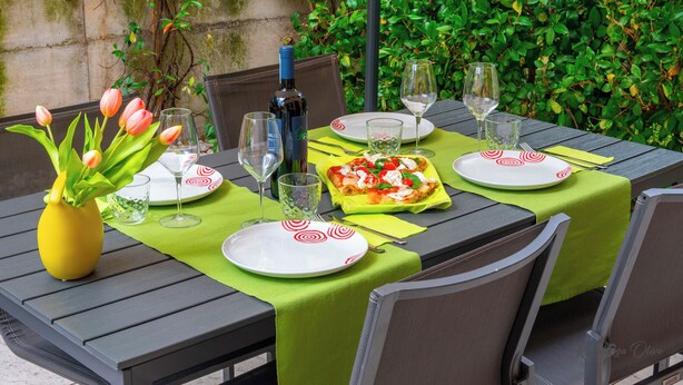 A dining table set with plates, glasses, a bottle, and a vase of flowers. - VALPOLICELLA APARTMENTS: OLIVE TREE RESIDENCE (Valgatara)