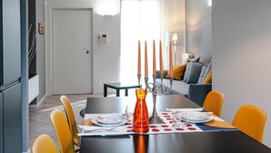 A dining area with a table set for two, a candle holder, and a view into a living room. - VALPOLICELLA APARTMENTS: OLIVE TREE RESIDENCE (Valgatara)