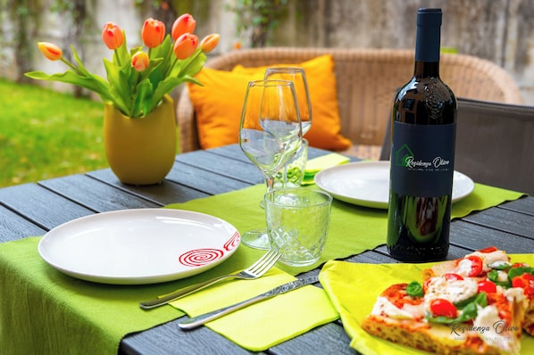 Et bord dækket med en vinflaske, et glas, en tallerken, en gaffel, en kniv, en serviet, et glas vand, en vase med tulipaner og et pizzastykke.