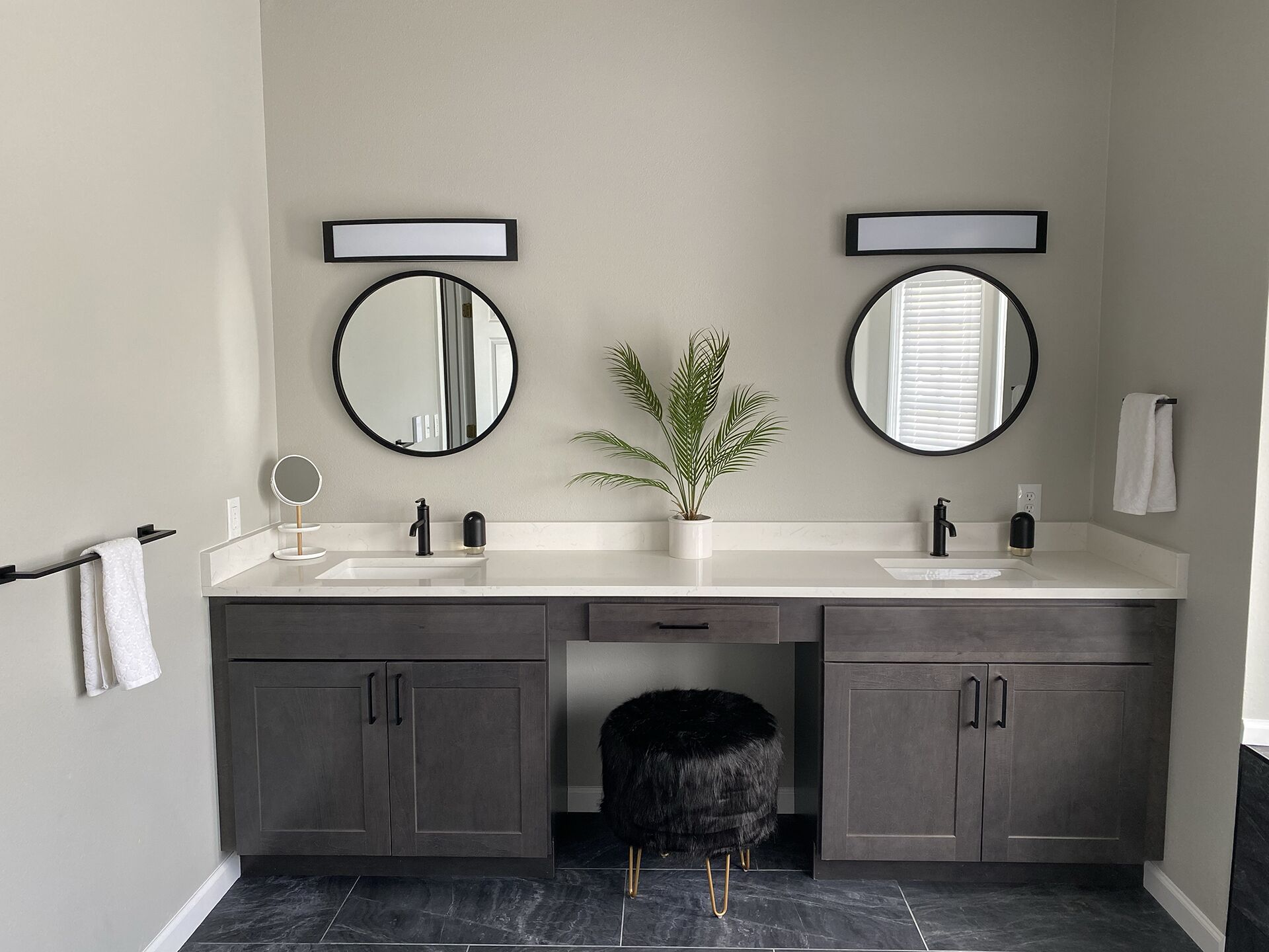 A modern bathroom with two sinks, dark cabinets, and a round mirror.