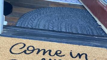 Un felpudo con el texto "Entra y acurrúcate" y una alfombra que conduce a una puerta.