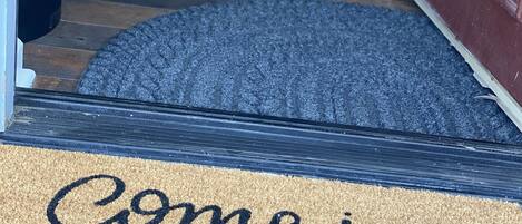 A doormat with the text "Come in and cozy up" and a rug leading to a door.