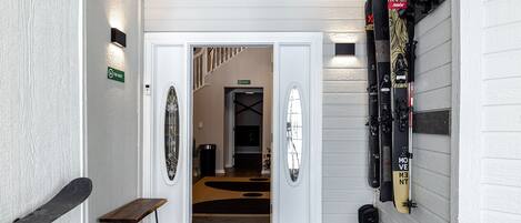 A hallway with a bench, a doormat, and skis mounted on the wall.