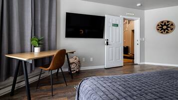 A hotel room with a bed, a desk with a chair, a television, a door with a sign, and a dartboard on the wall.