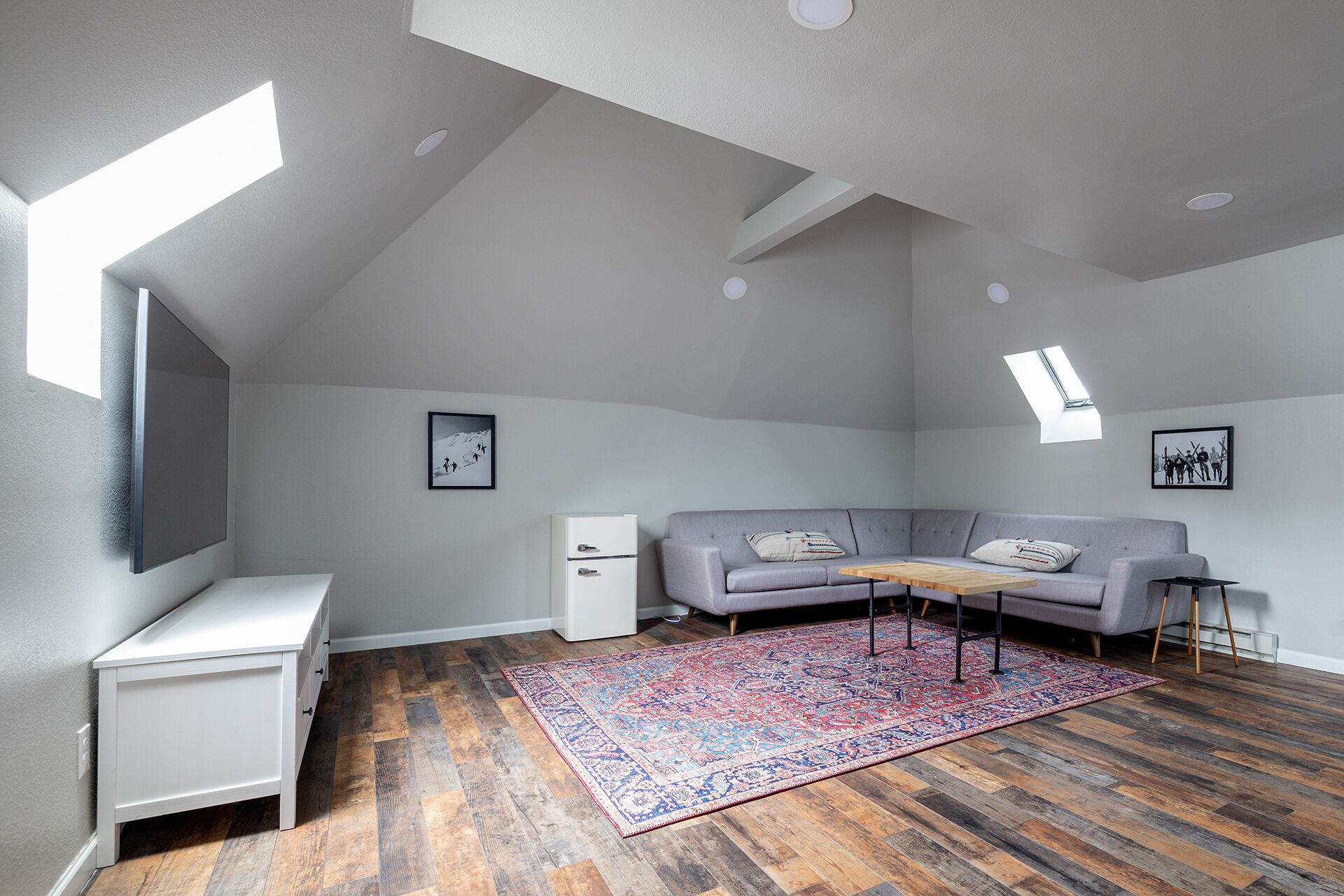 A loft-style room with a gray sofa, a small white desk, and a colorful rug.