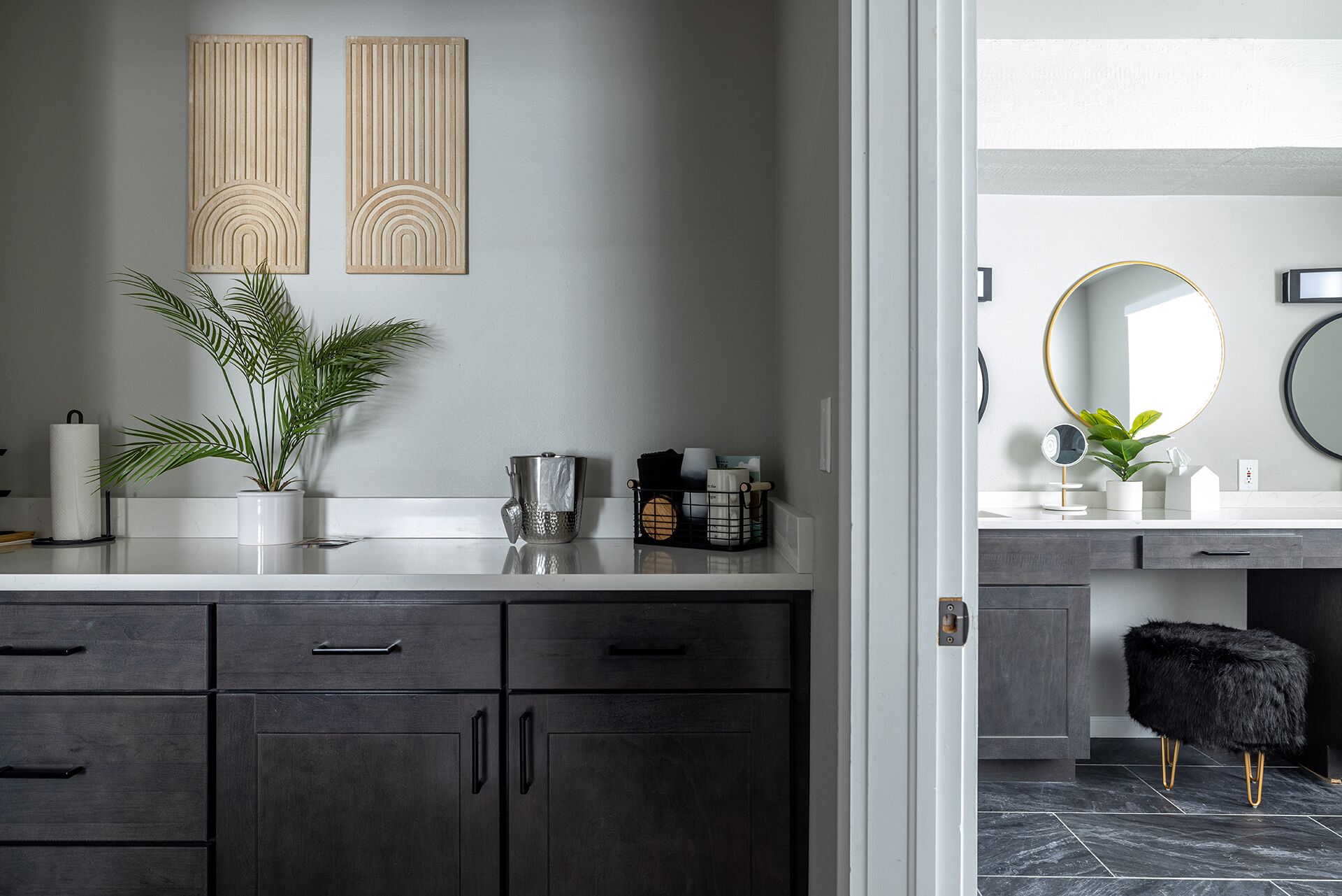 A modern bathroom with dark wood cabinets, a white countertop, and a mirror with a gold frame.