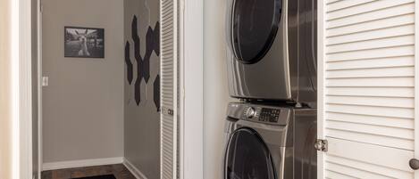 Une buanderie équipée de deux machines à laver et deux sèche-linge à chargement frontal superposés, d’un tapis noir sur le sol et d’un tableau représentant un lama accroché au mur.