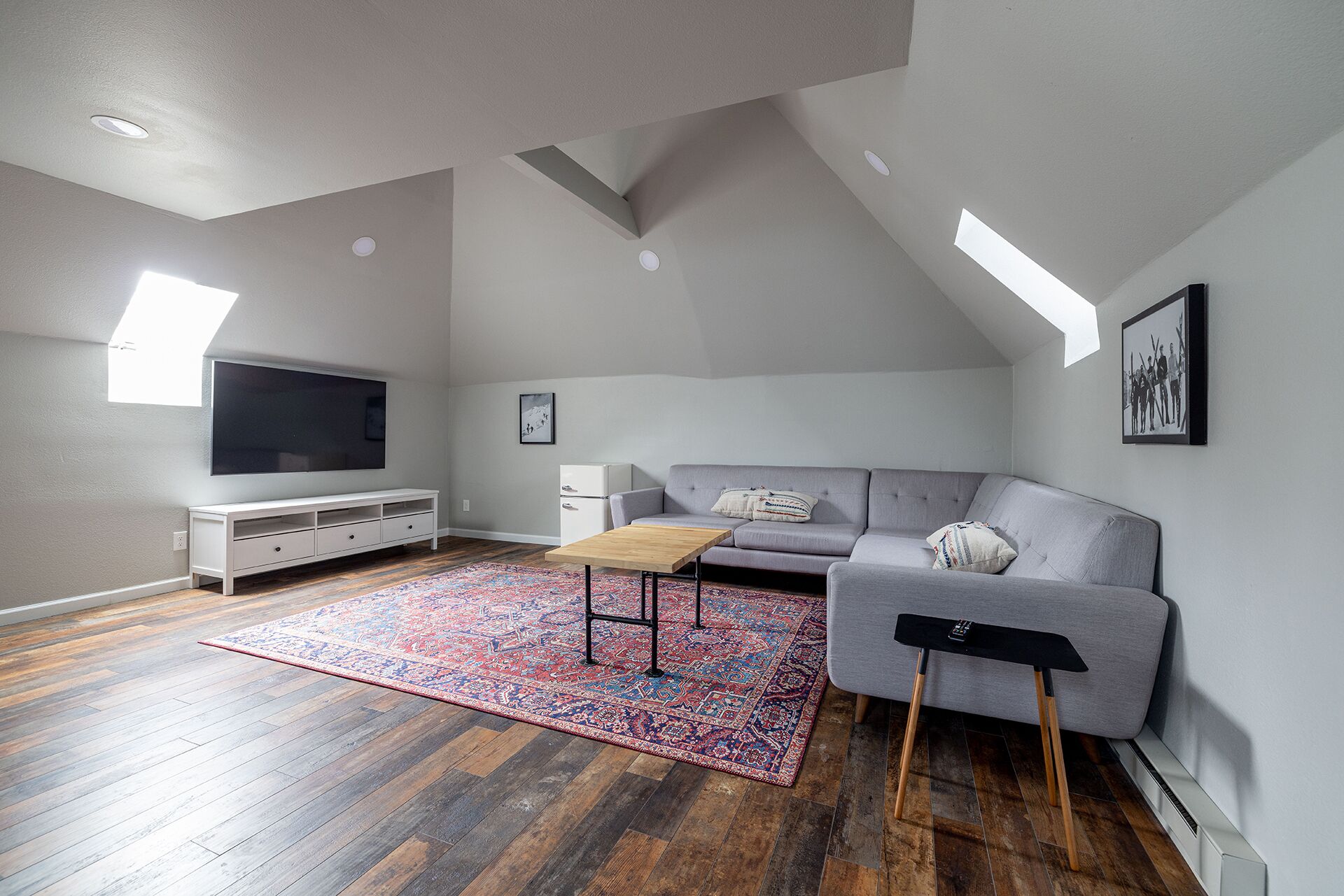 Una sala de estar moderna con un sofá gris, un televisor de pantalla plana, una mesa de centro de madera y una alfombra estampada.