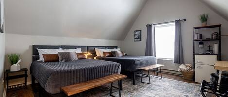 Quarto com duas camas, um banco, uma escrivaninha e uma janela com cortinas.