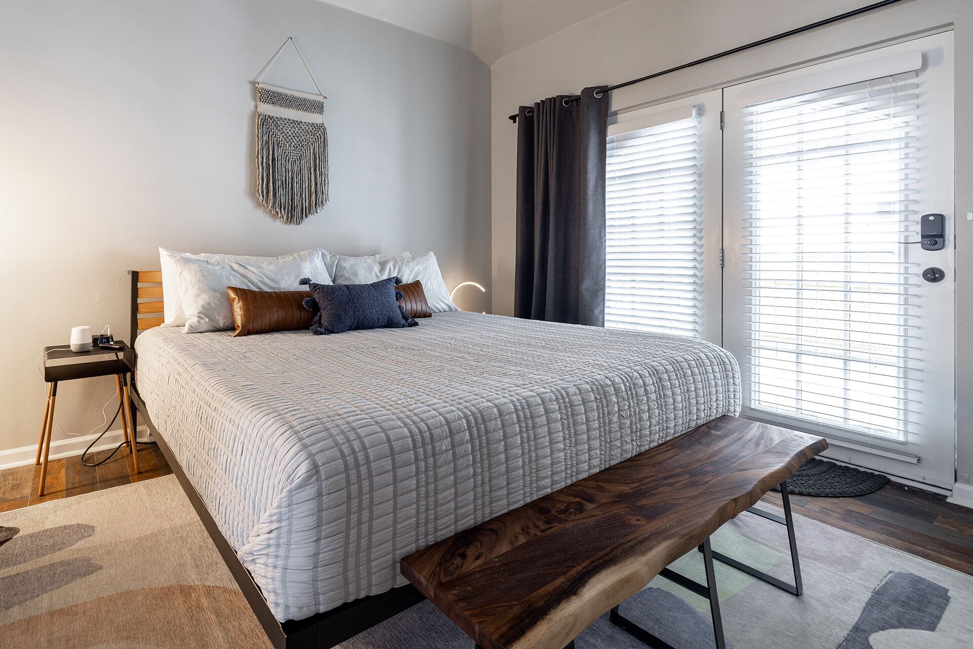 A neatly arranged bedroom with a bed, bedside table, bench, and a wall-mounted decor piece.