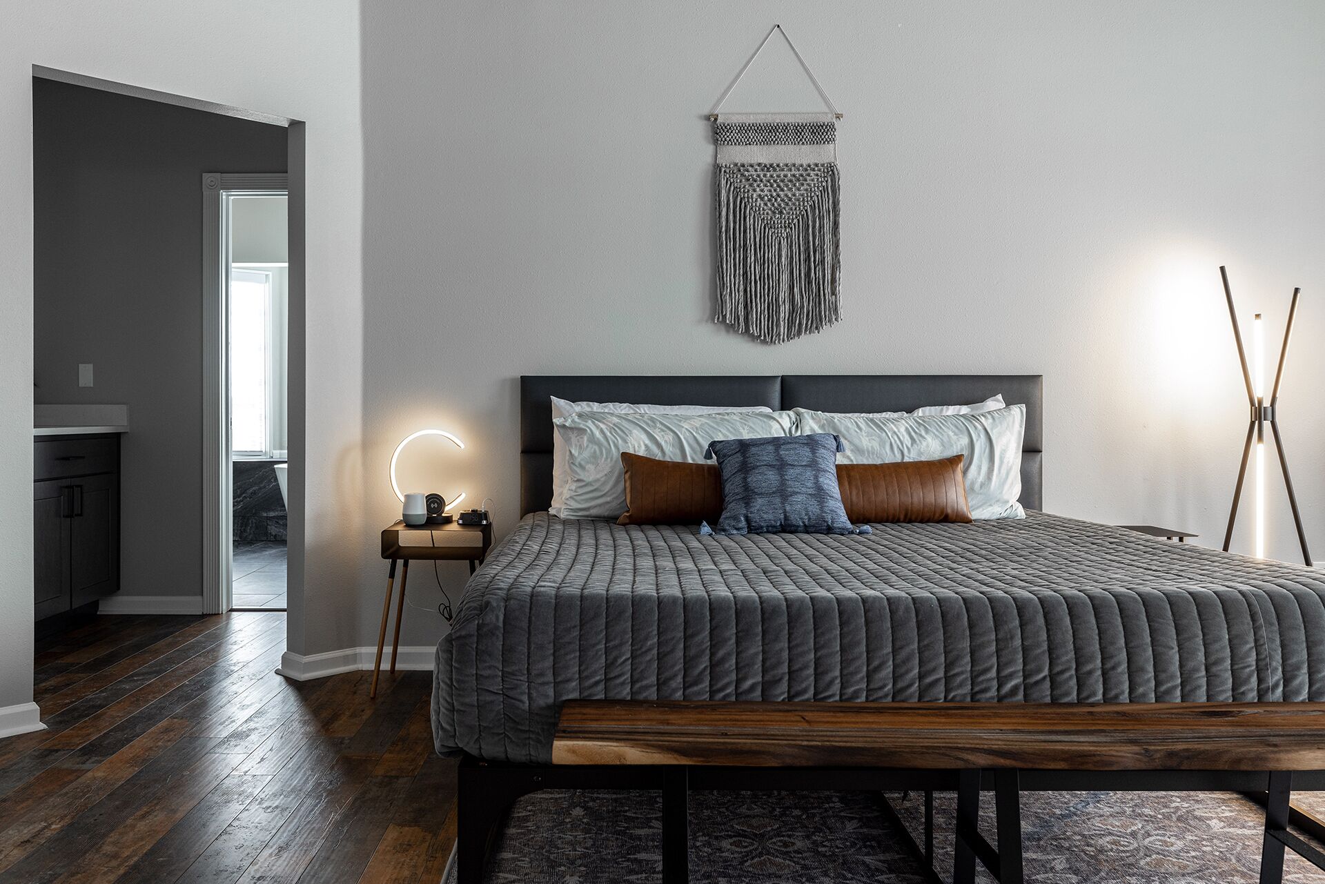 A bedroom with a bed, bedside table, and a wall-mounted macrame piece.