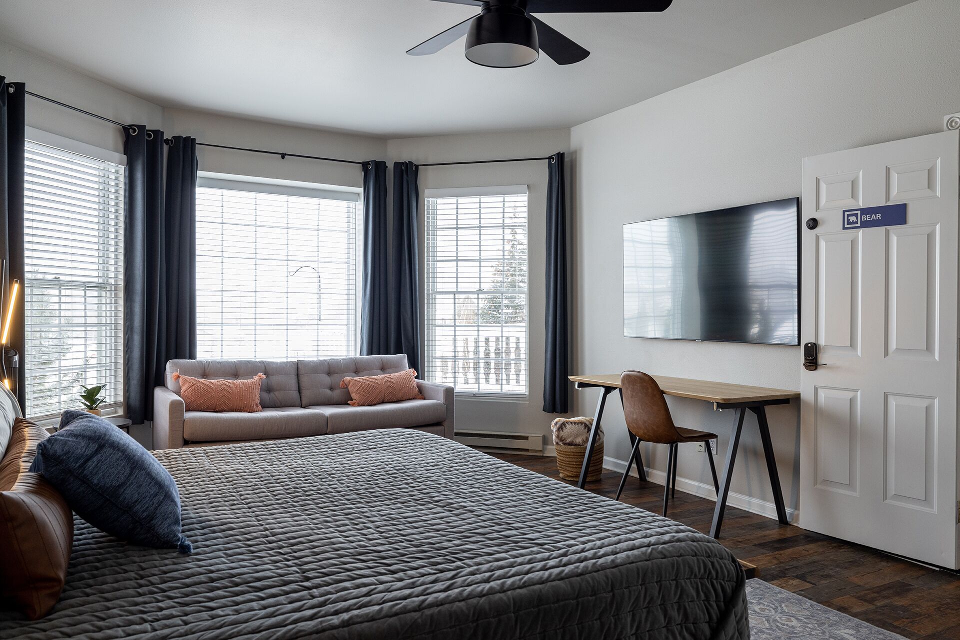 A modern bedroom with a bed, a sofa, a desk, and a TV.