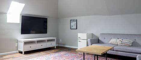 Ein modernes Wohnzimmer mit einem grauen Sofa, einem Holztisch, einer weißen TV-Konsole und einem gemusterten Teppich.