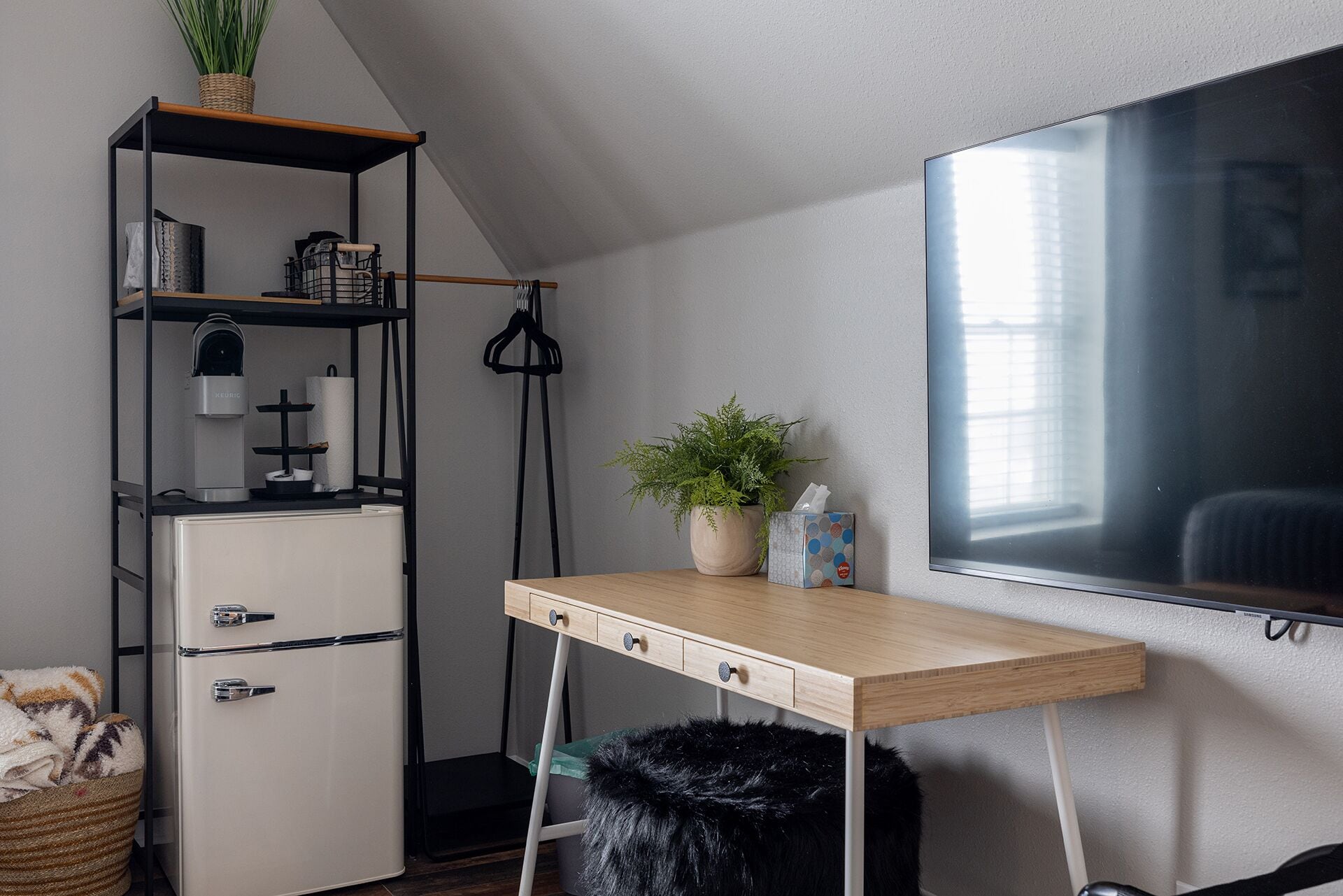 Una habitación compacta y moderna con escritorio, ventanal amplio, armario empotrado y una pequeña planta.